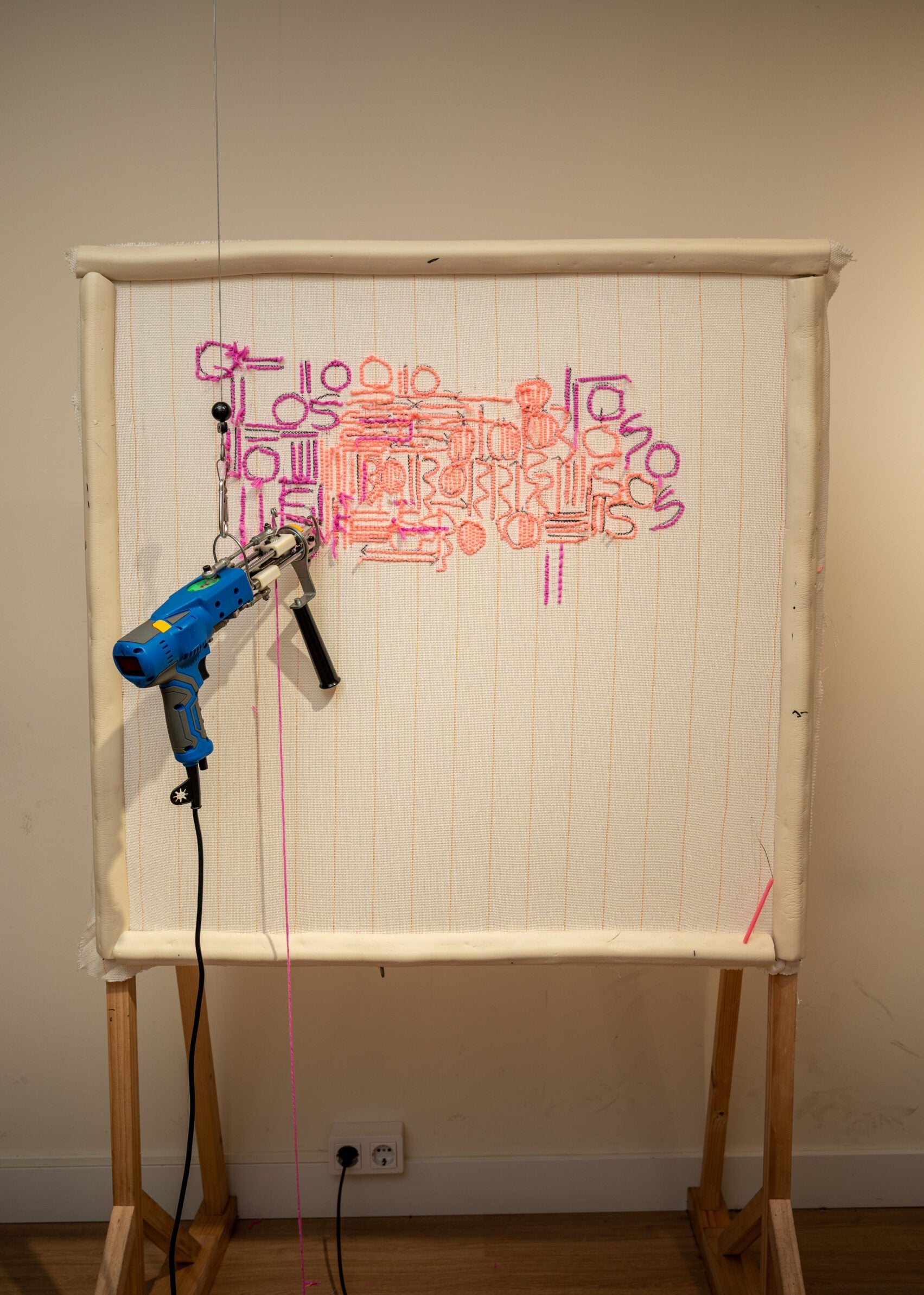 Whiteboard with colorful text and a blue drill on a wooden stand against a plain wall.