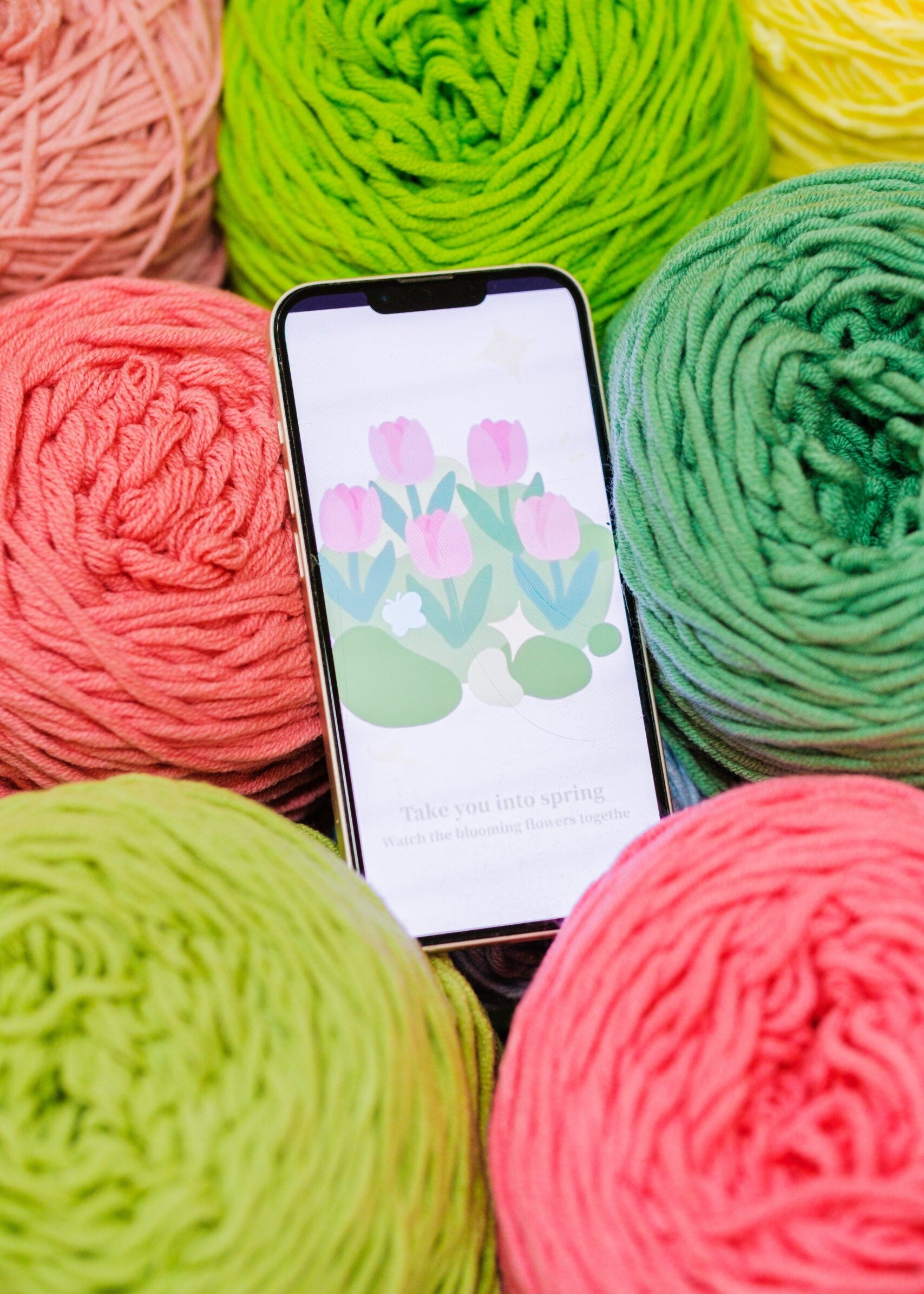 Smartphone displaying a floral app interface with colorful yarn balls in the foreground.