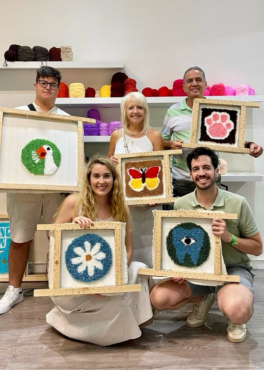 Group of people holding framed artworks with various designs in a room.