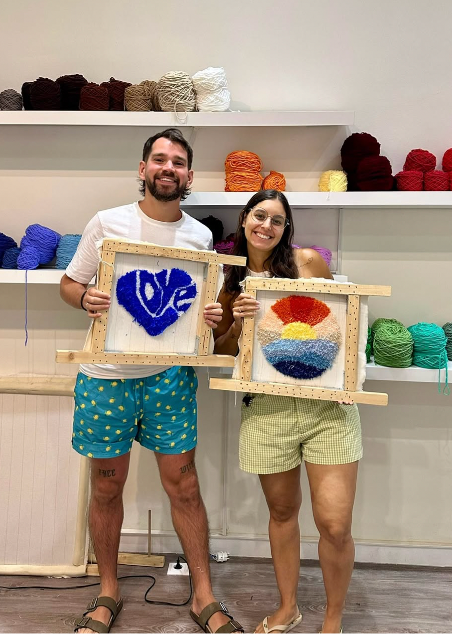 Two people holding framed artworks in a yarn store.