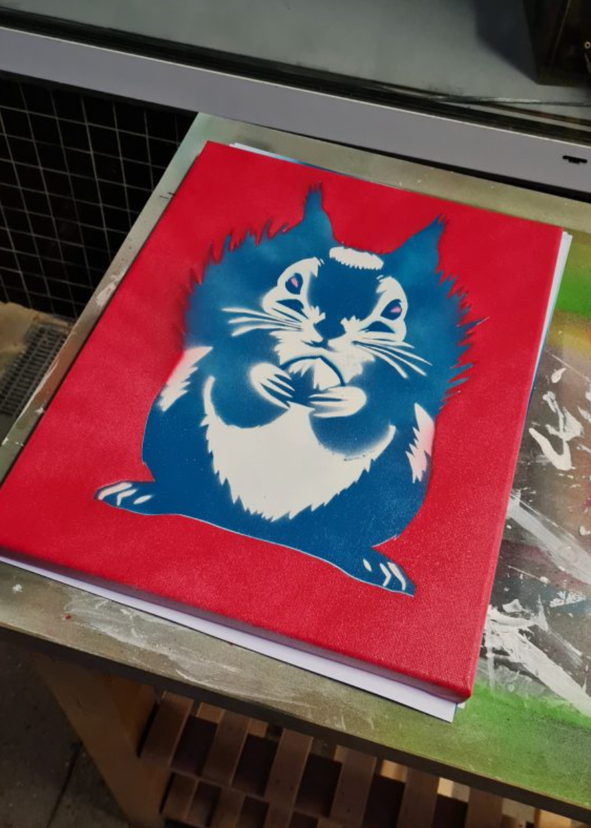 A square red canvas print featuring a stylized blue and white cat illustration, displayed on a wooden table.