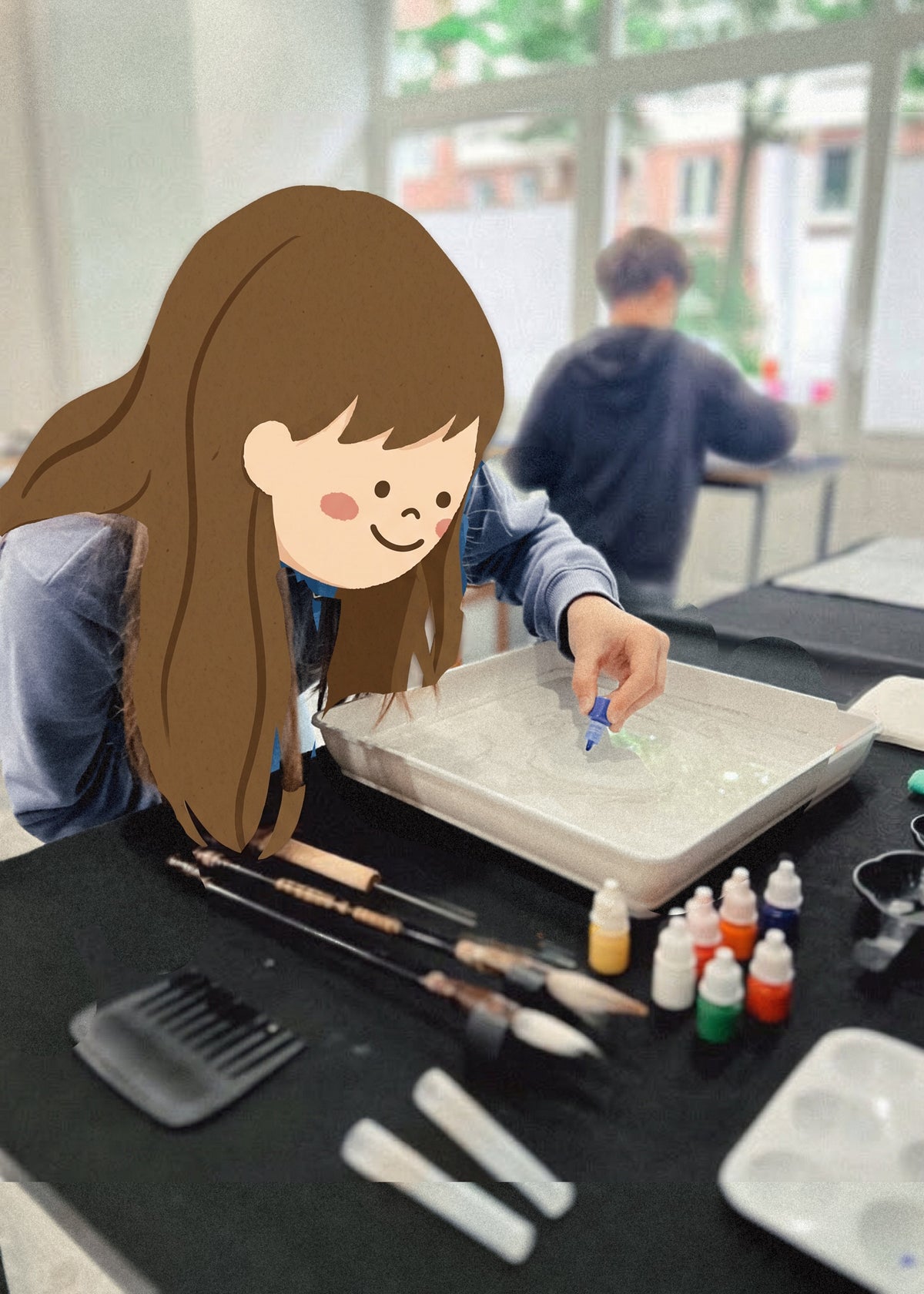 A person with long brown hair is shown from the side, using a small blue tool in a tray of water on a table covered with painting supplies, including brushes, paint bottles, and a palette. Another person is blurred in the background near a window.
