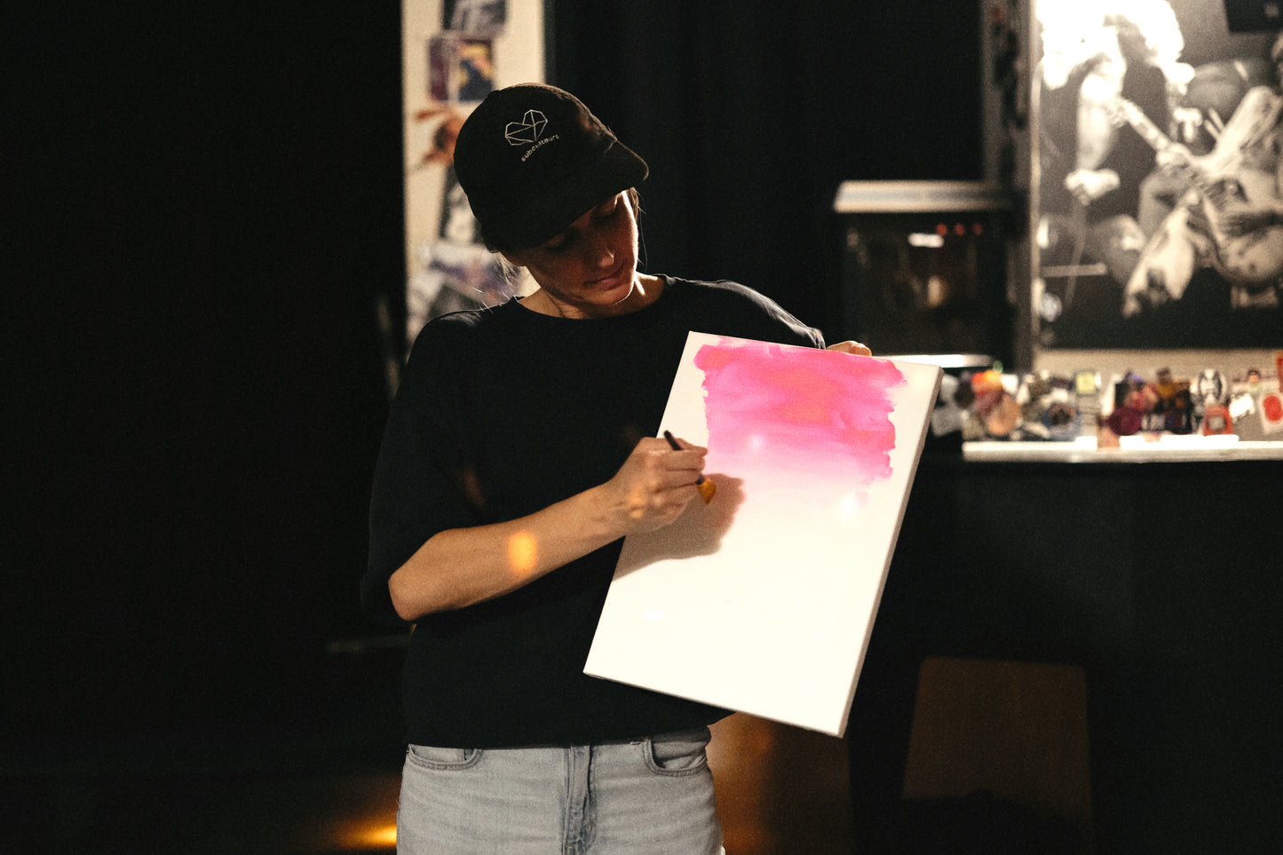 Person holding a painting with pink and white gradient in a dark room.