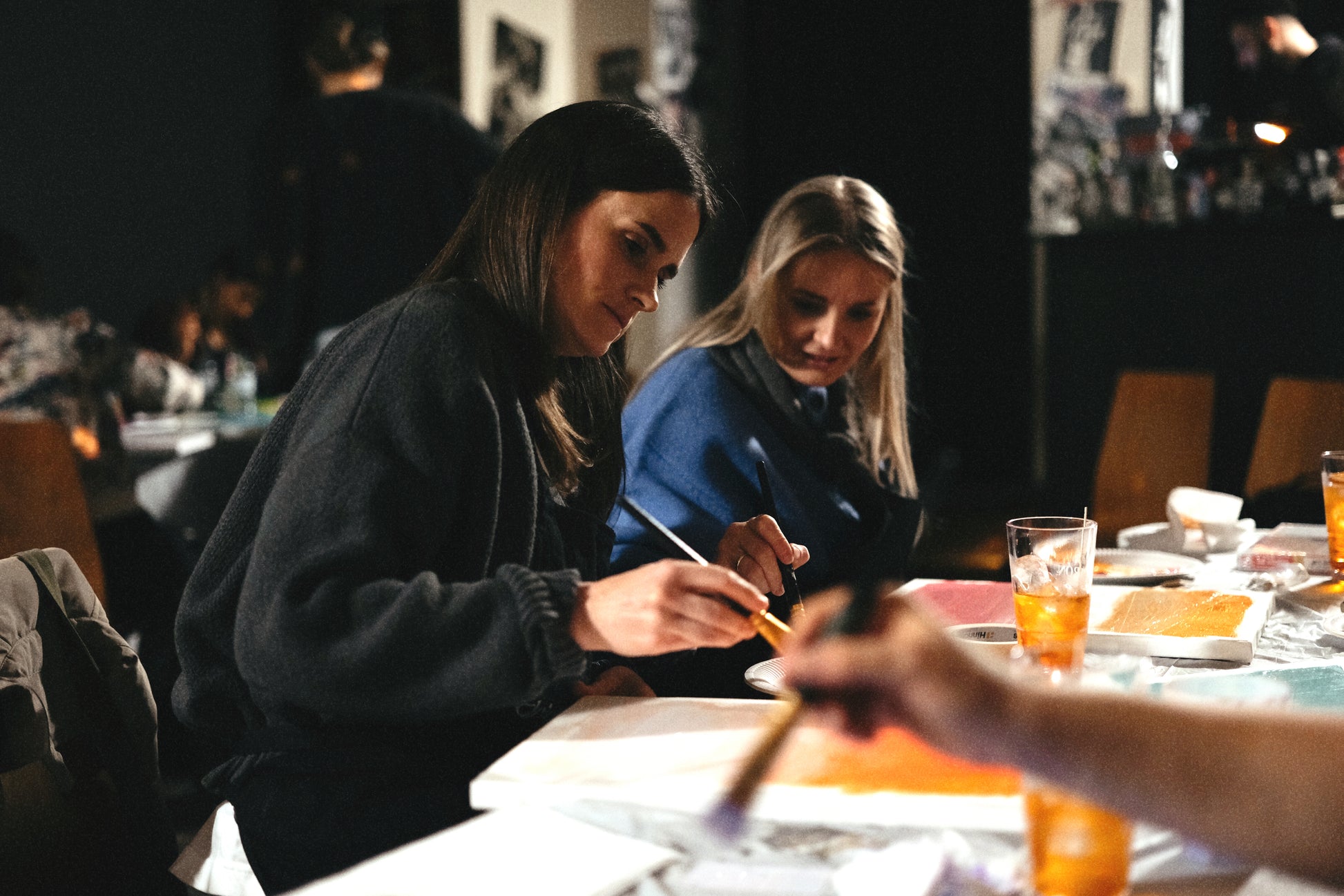 Two women sitting at a table with drinks, engaged in an activity.