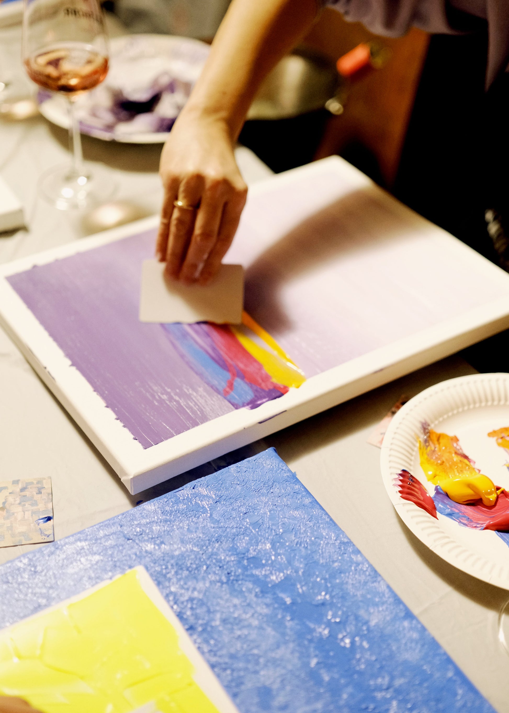 Person painting on a canvas with a palette and glass of wine in the background