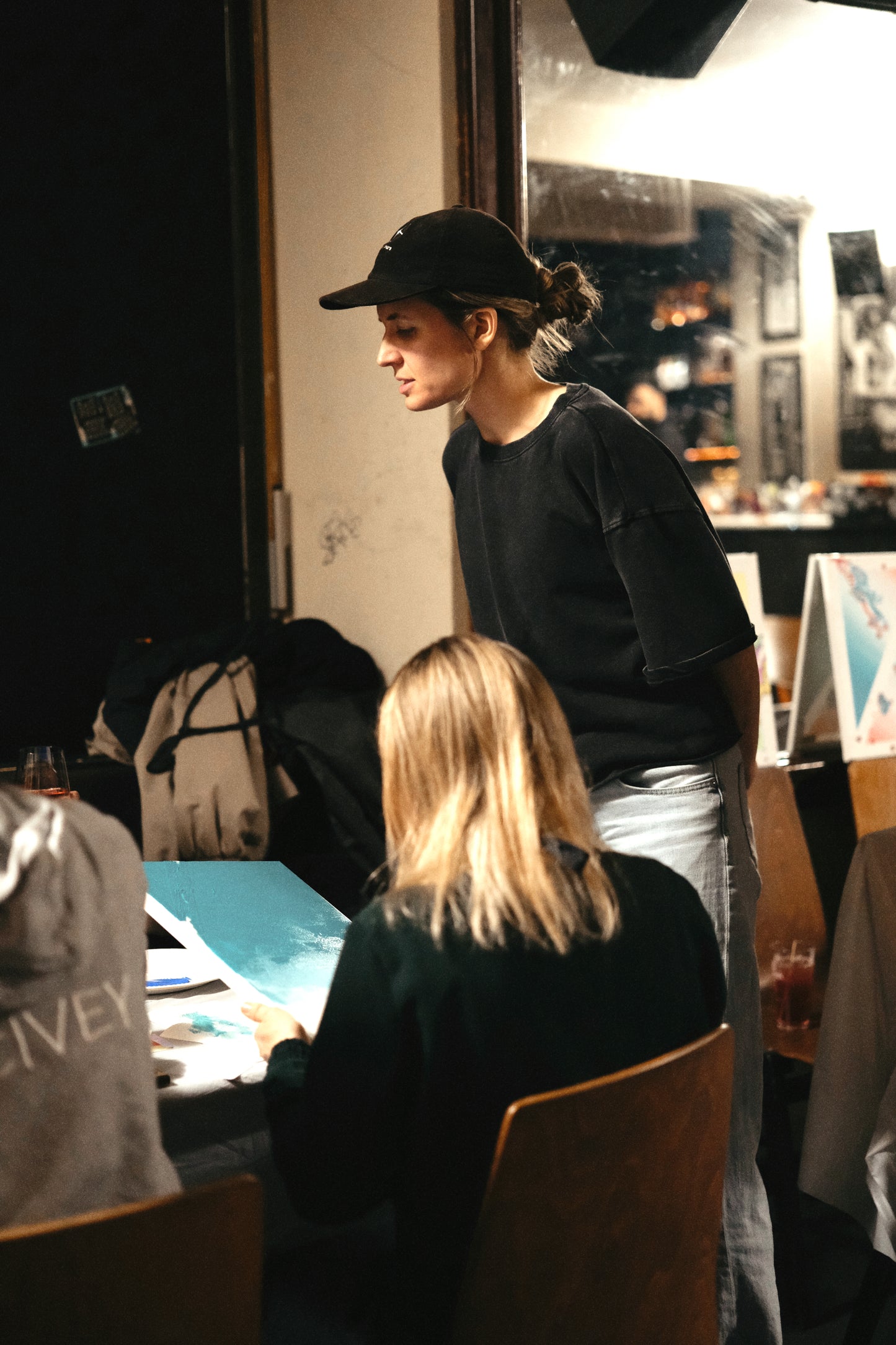 Person wearing a black cap and black shirt standing in a room with tables and chairs.