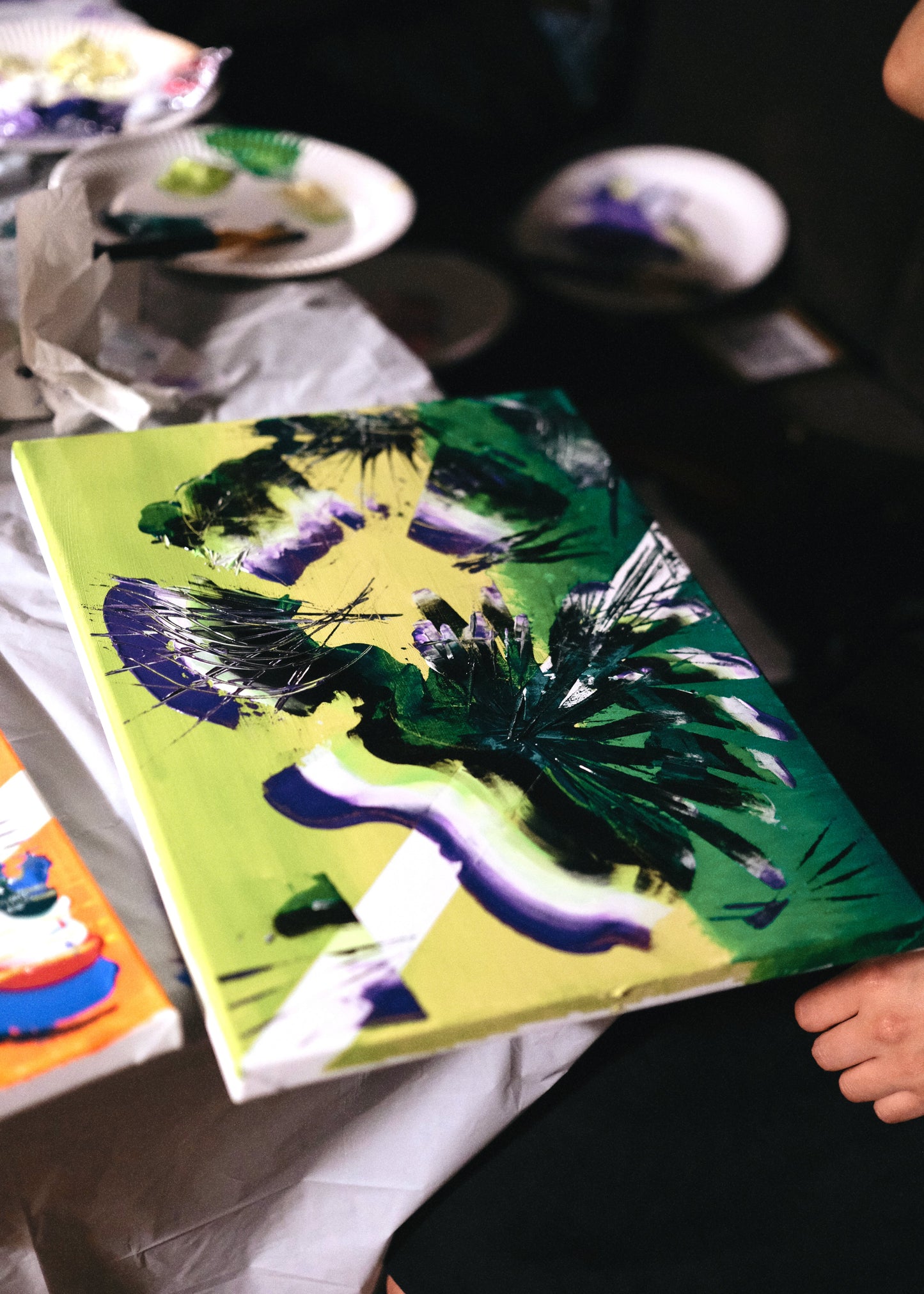 Person holding a colorful painting of a face with green and purple accents.