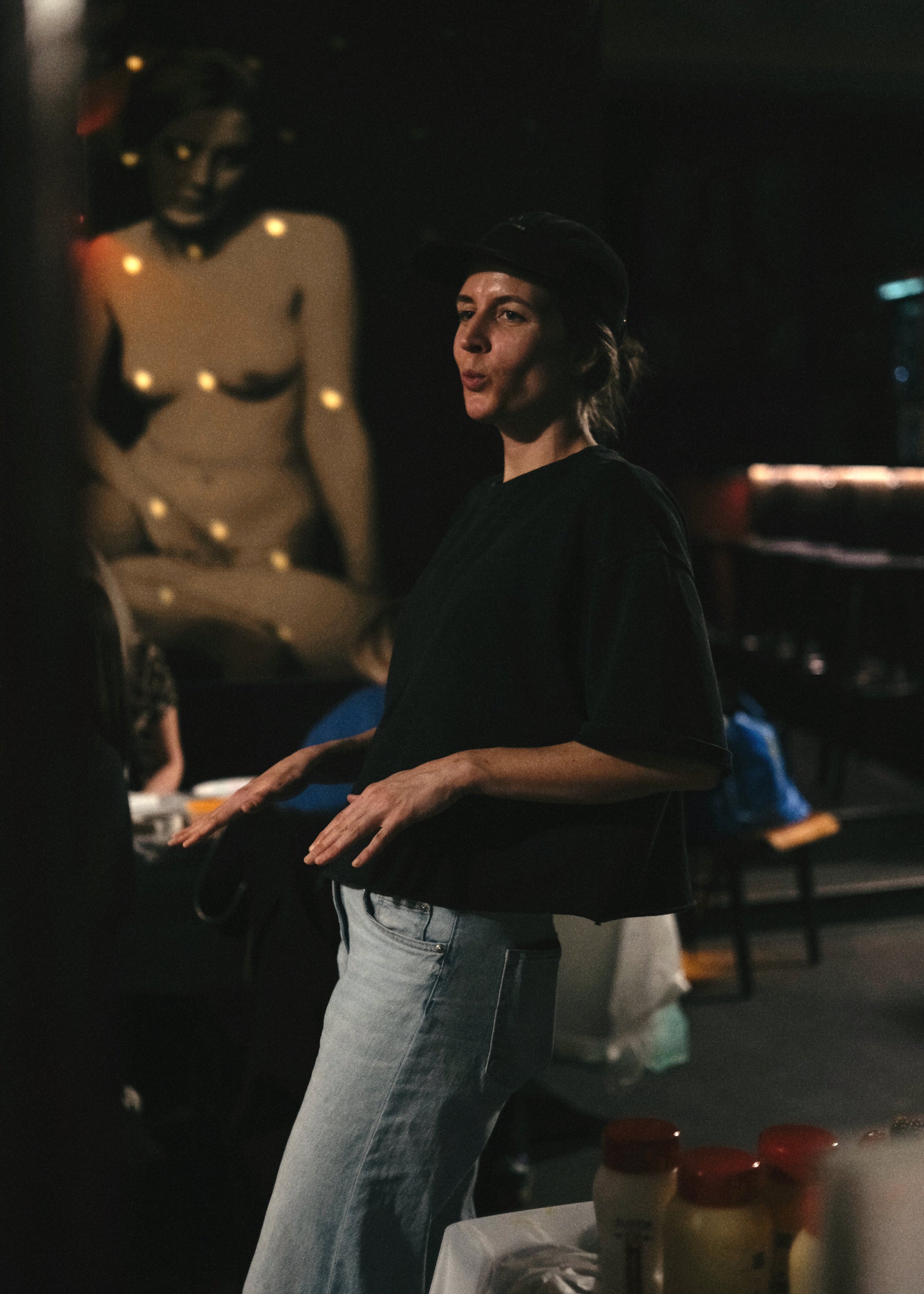 Person standing in a dimly lit room with a painting in the background
