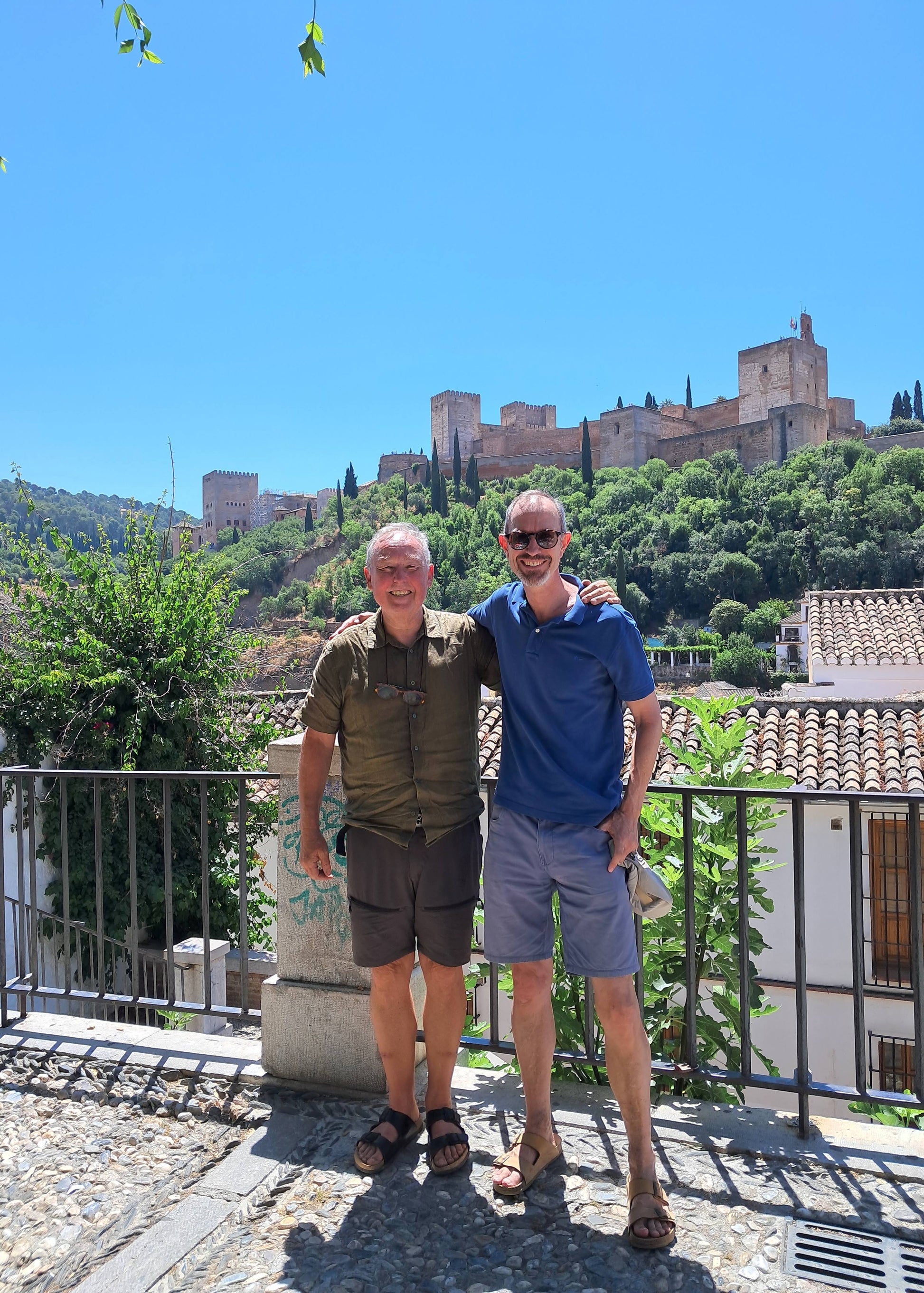 Two men standing on a scenic overlook with a castle in the background