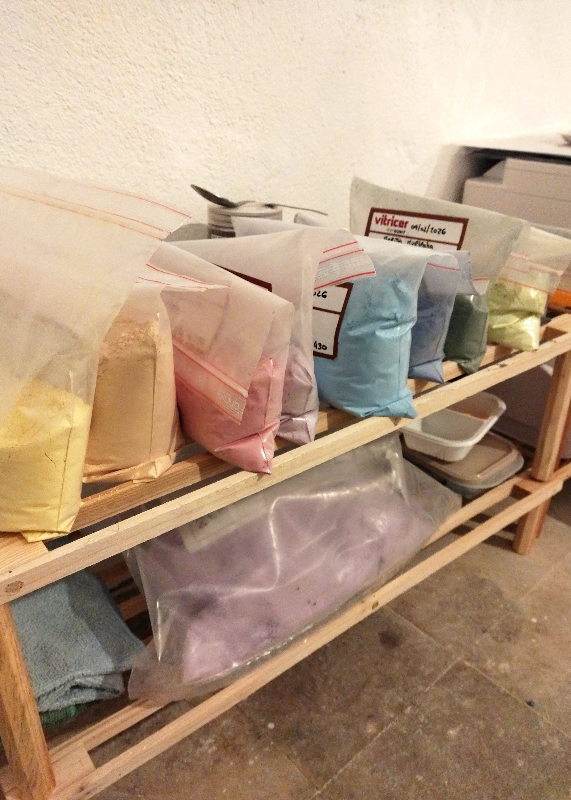 Wooden shelf with bags of colorful powders on a concrete floor.