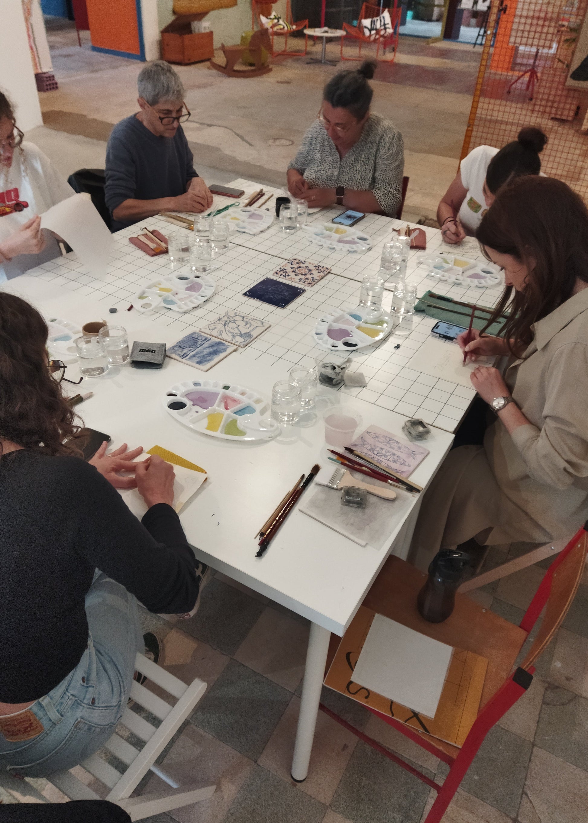 Group of people sitting around a table with art supplies in a casual setting