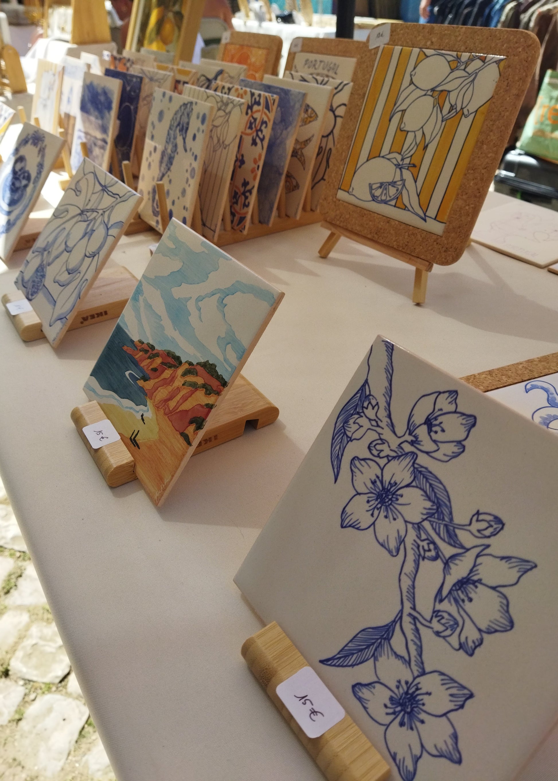 Small artworks on easels with floral and landscape designs at an outdoor market.