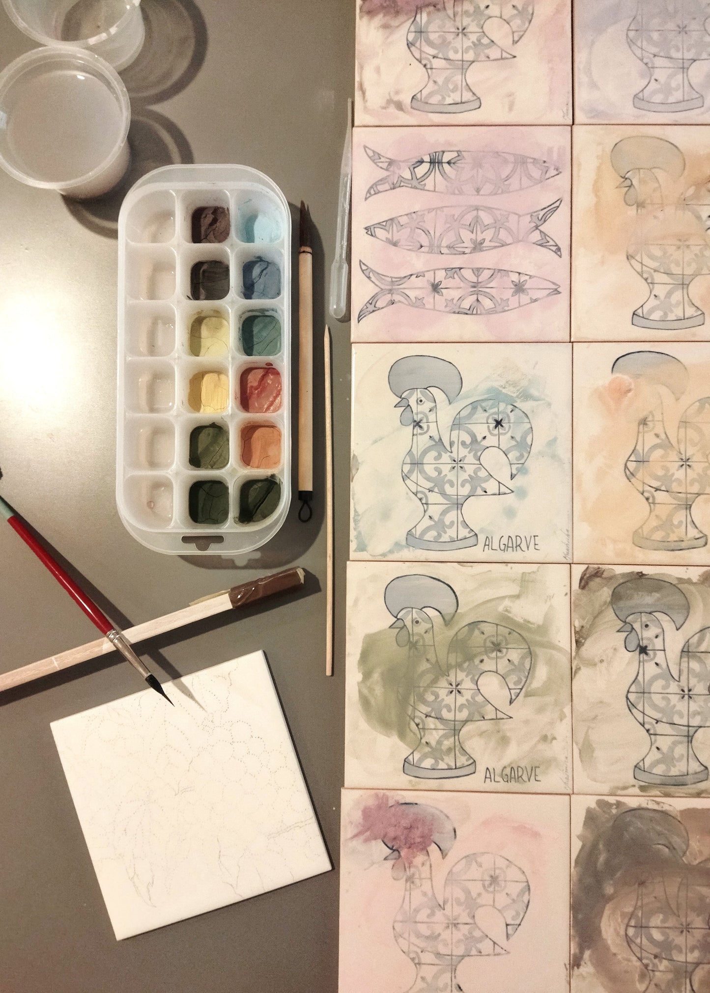Art supplies including watercolor paints, brushes, and a watercolor paper next to illustrated characters on a grid.