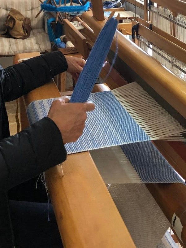 Person weaving blue fabric on a loom with a focus on the hands and materials.
