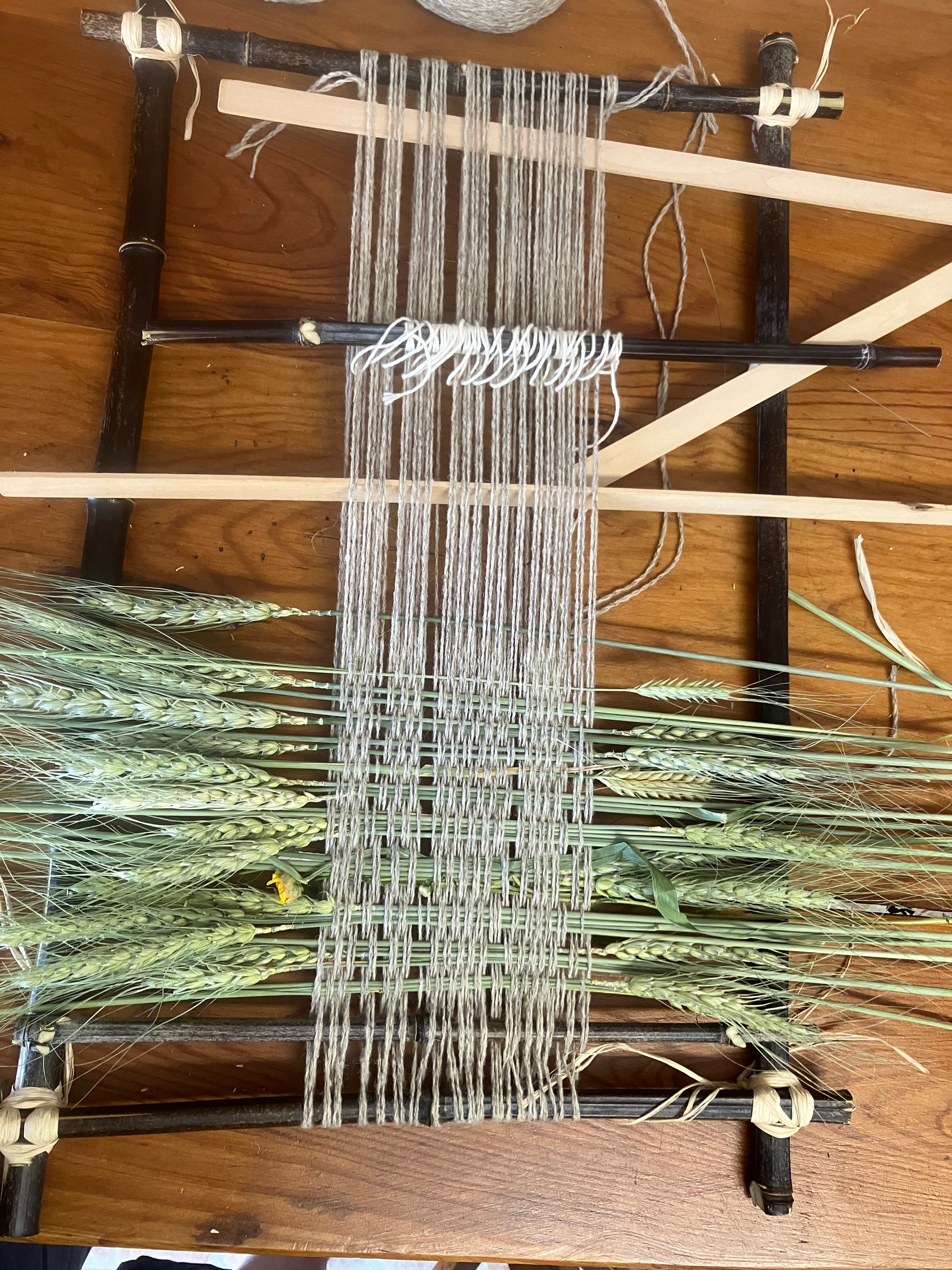 Weaving loom with threads and green materials on a wooden surface