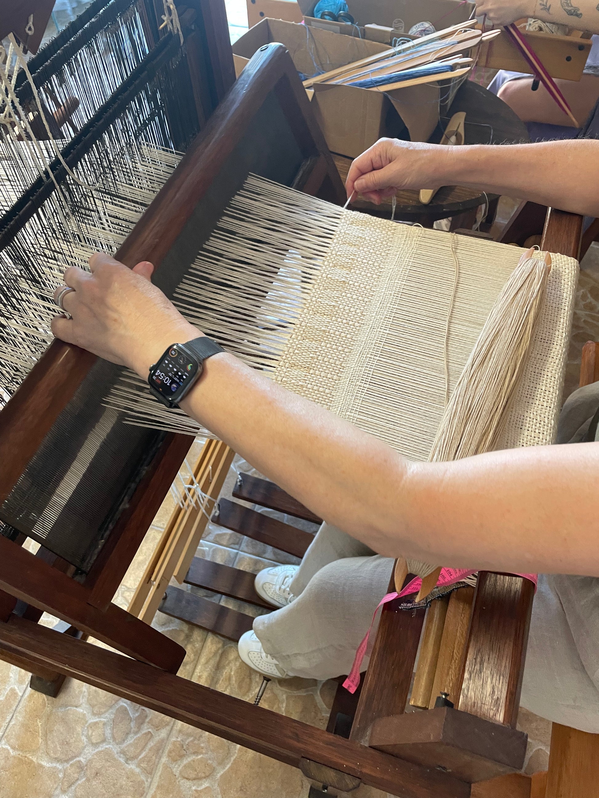 Person weaving on a loom with a focus on hands and materials.
