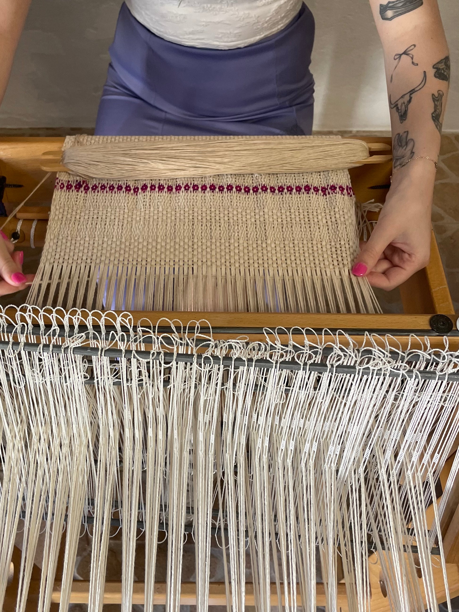 Person weaving on a loom with a focus on the fabric and tools.