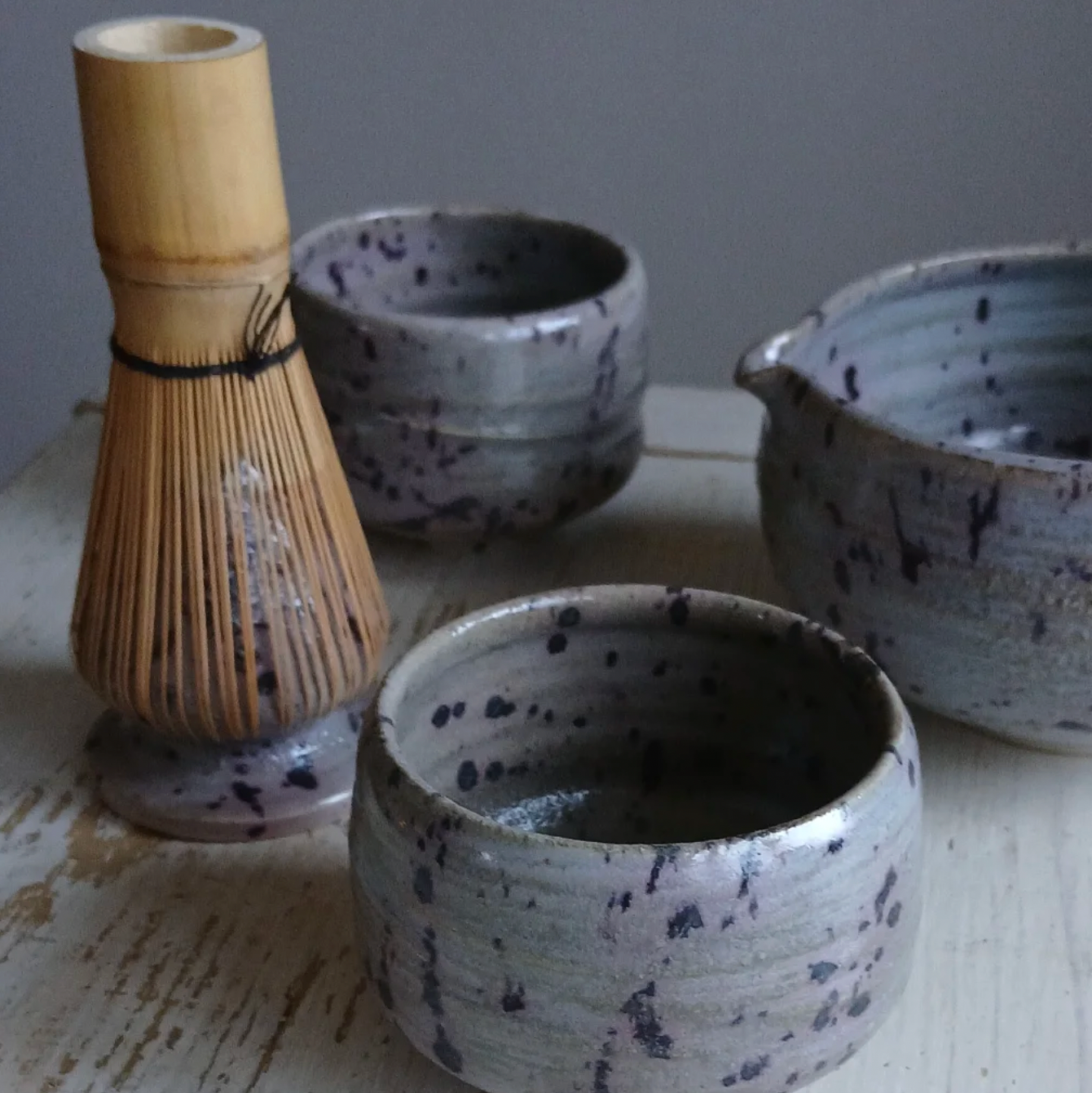 Set of ceramic tea bowls and a whisk on a wooden surface