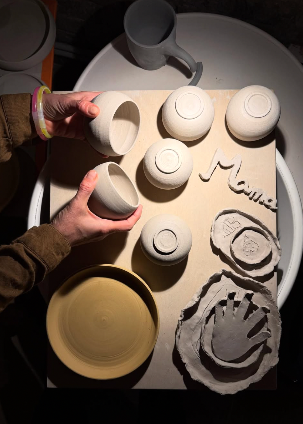 Person holding a ceramic bowl next to other ceramic pieces on a table with a 'Mamie' branding.