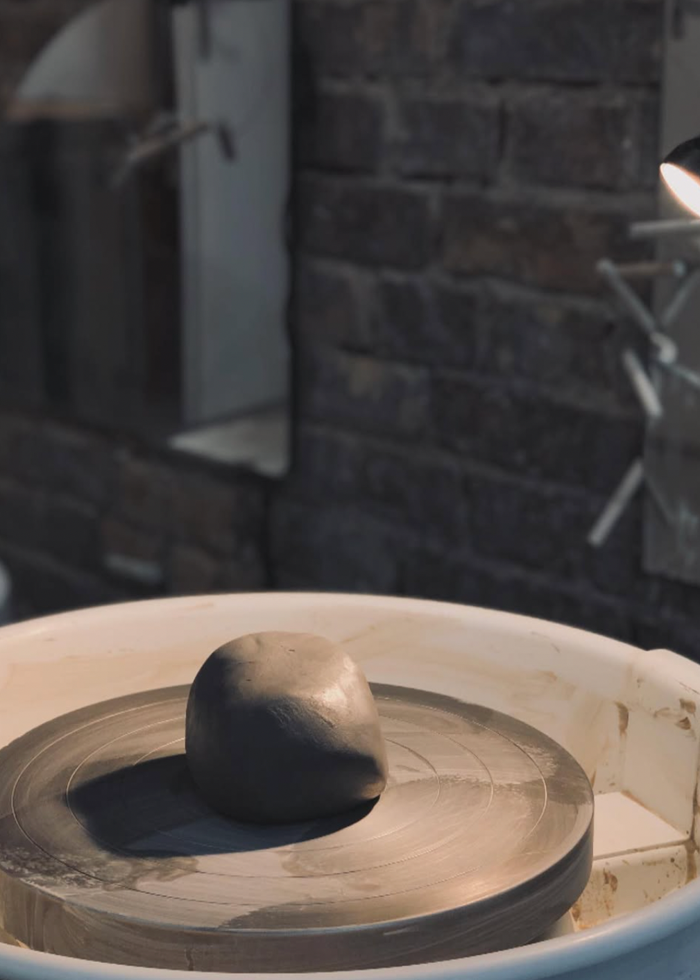 Clay potter's wheel with a piece of clay on it, set against a stone wall.