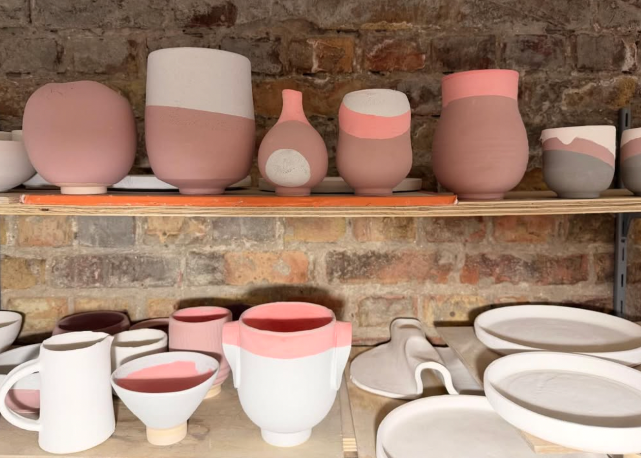 Collection of ceramic pots and bowls with pink and white glaze on a stone wall background