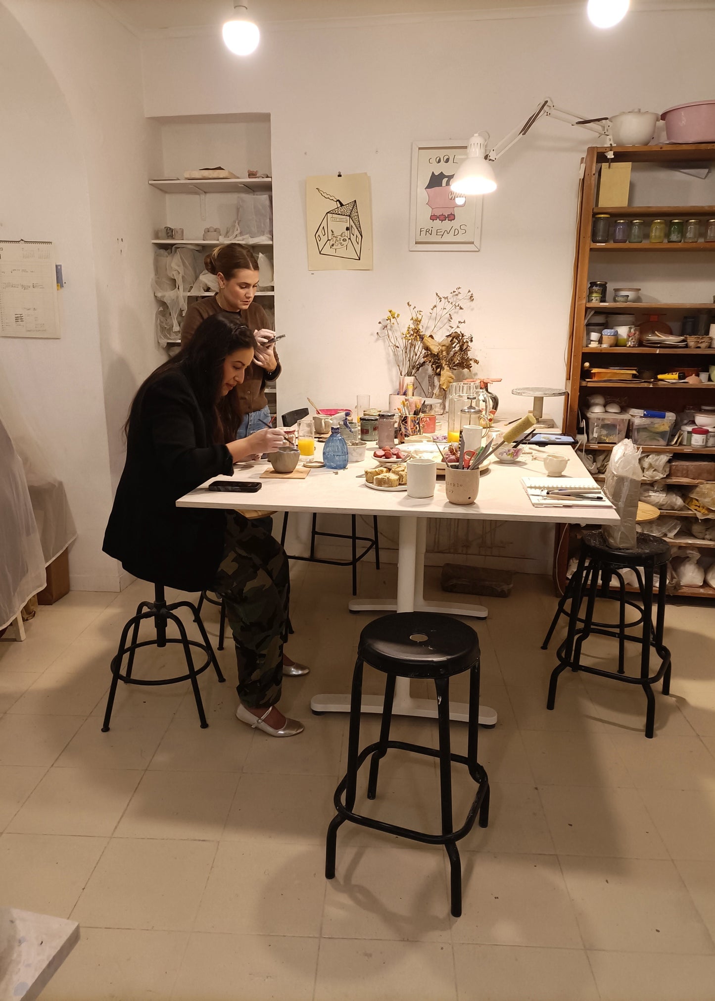 Two people sitting at a table in a cozy room with shelves and decor.