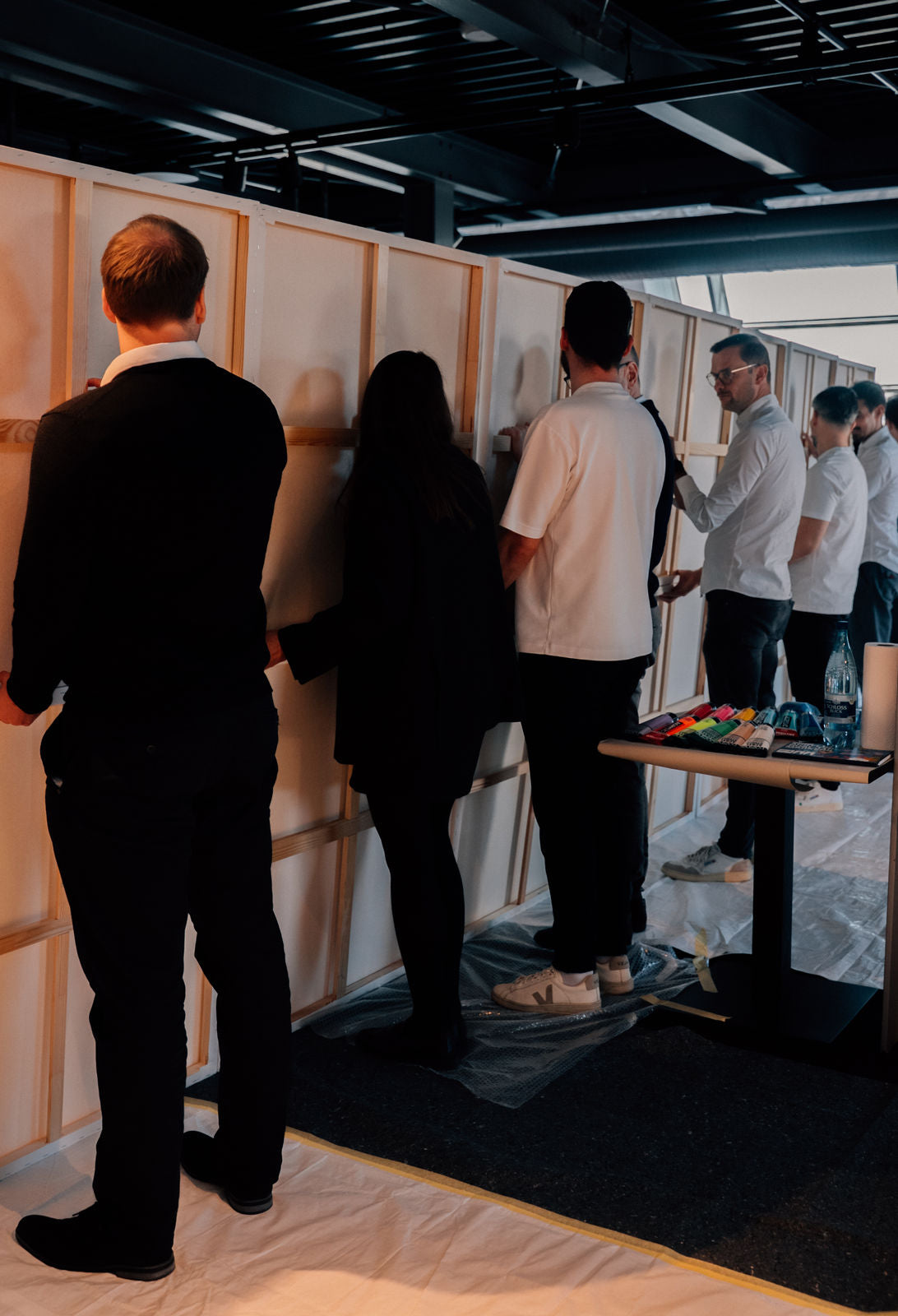 Group of people standing around a table with art supplies in an indoor setting