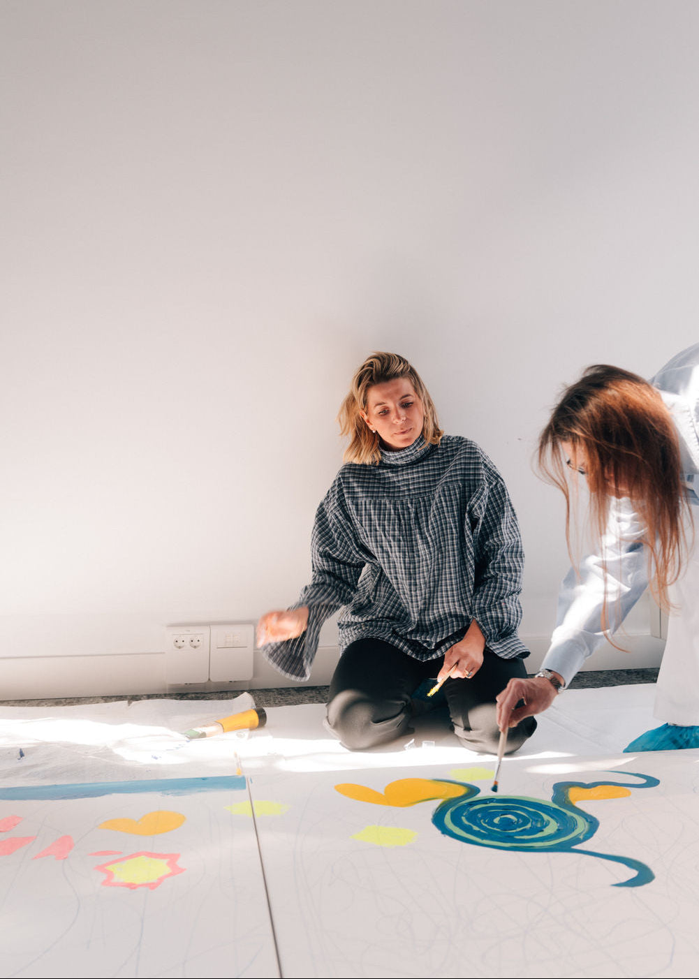 Two people sitting on a white floor with colorful drawings.
