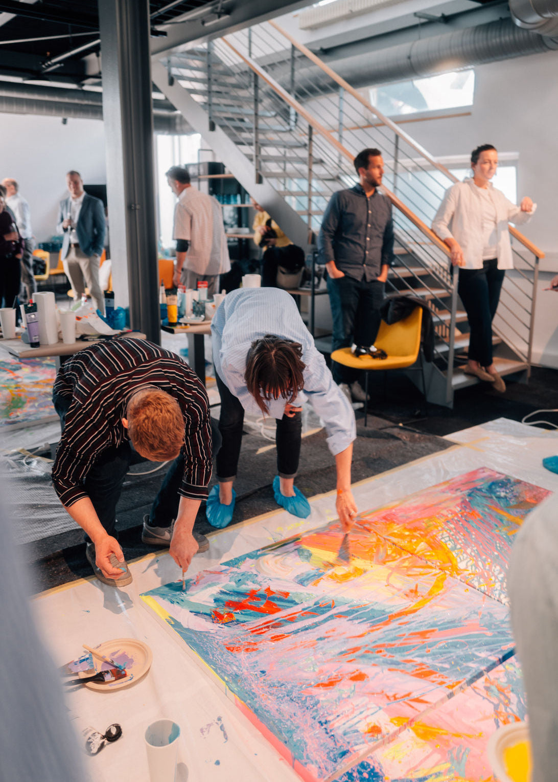 Group of people working on a large abstract painting in a modern office setting.