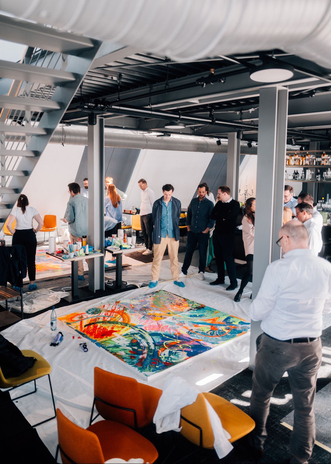 Group of people gathered around a table with a colorful painting in a modern indoor setting.