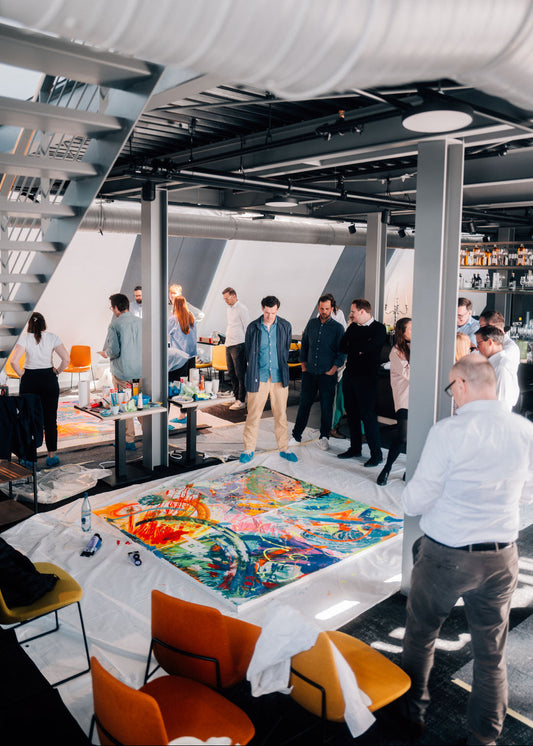 Group of people gathered around a table with a colorful painting in a modern indoor setting.