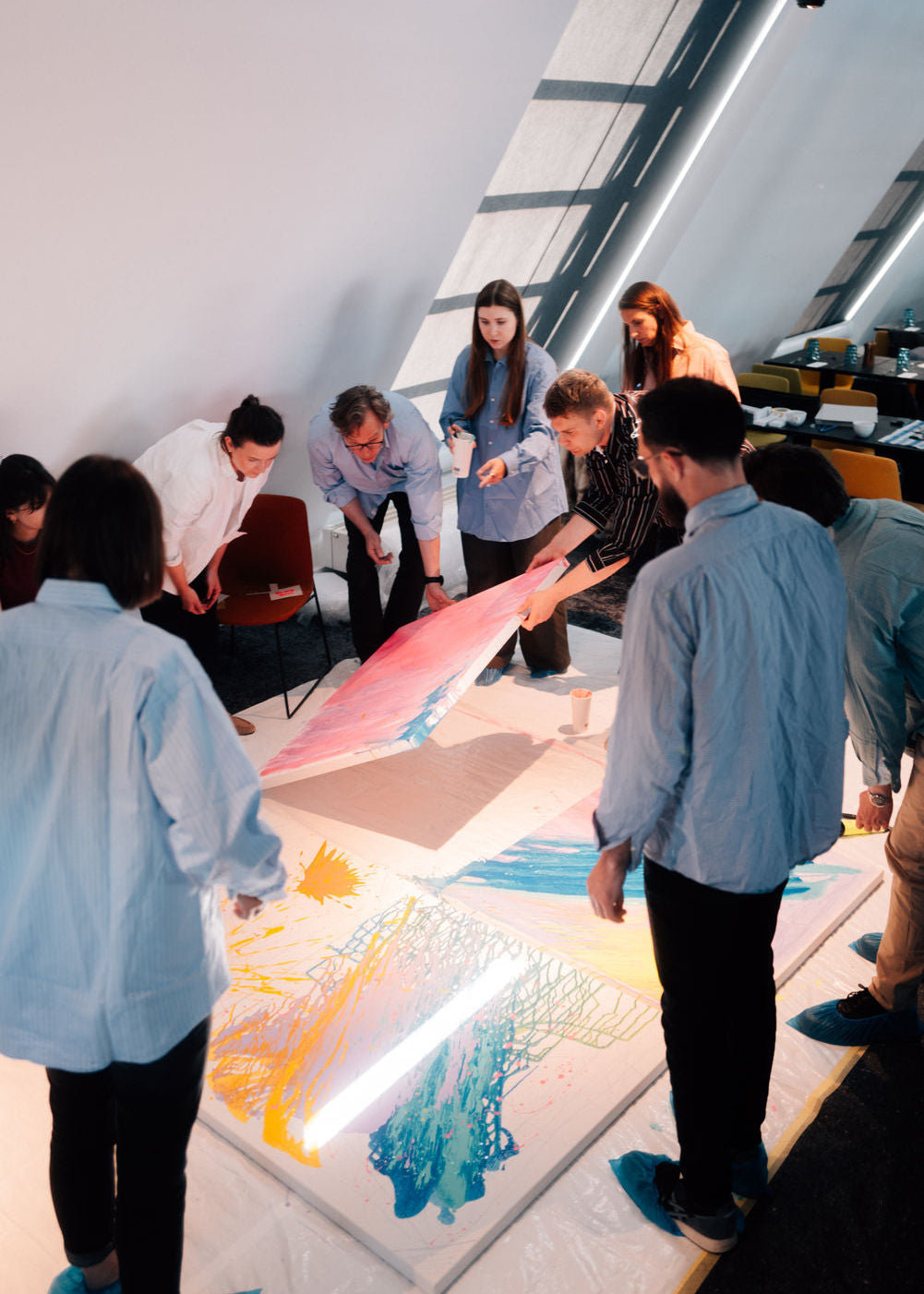 Group of people collaborating on a large colorful painting in a modern indoor setting.
